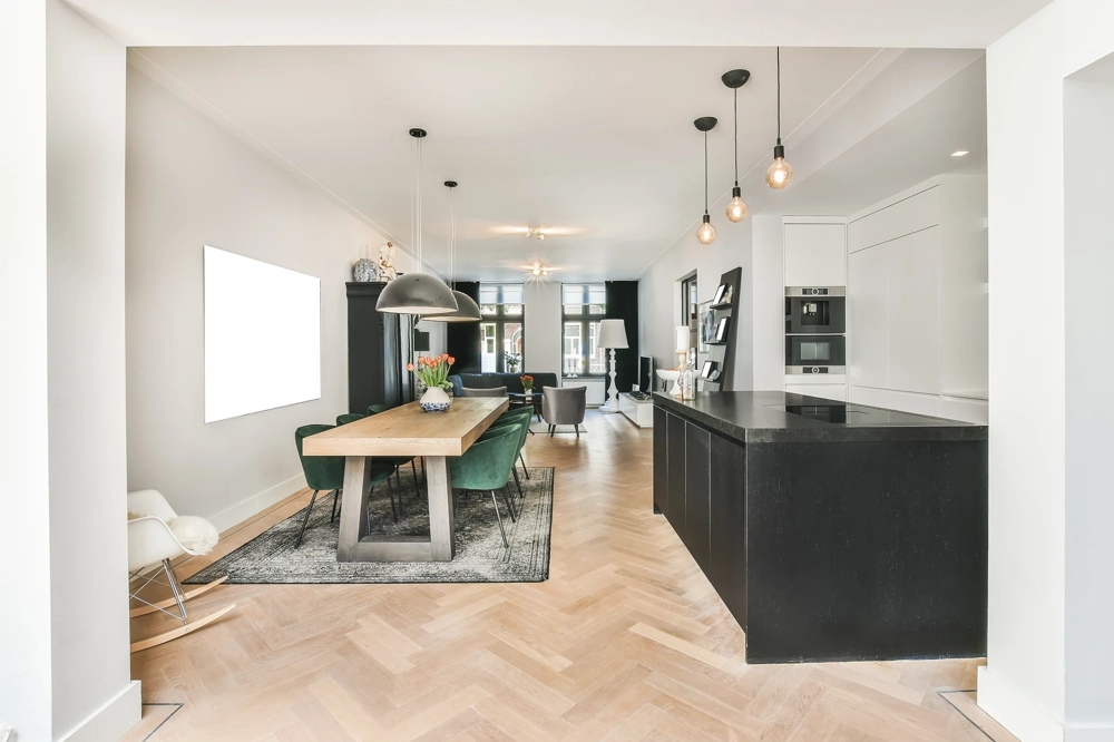 Remont kuchni otwartej z czarną wyspą, drewnianym stołem, zielonymi krzesłami i jodełkowym parkietem