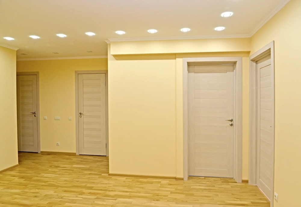 Przestronny pokój z beżowymi ścianami, sufitami podwieszanymi z oświetleniem LED i podłogą z paneli Układanie paneli