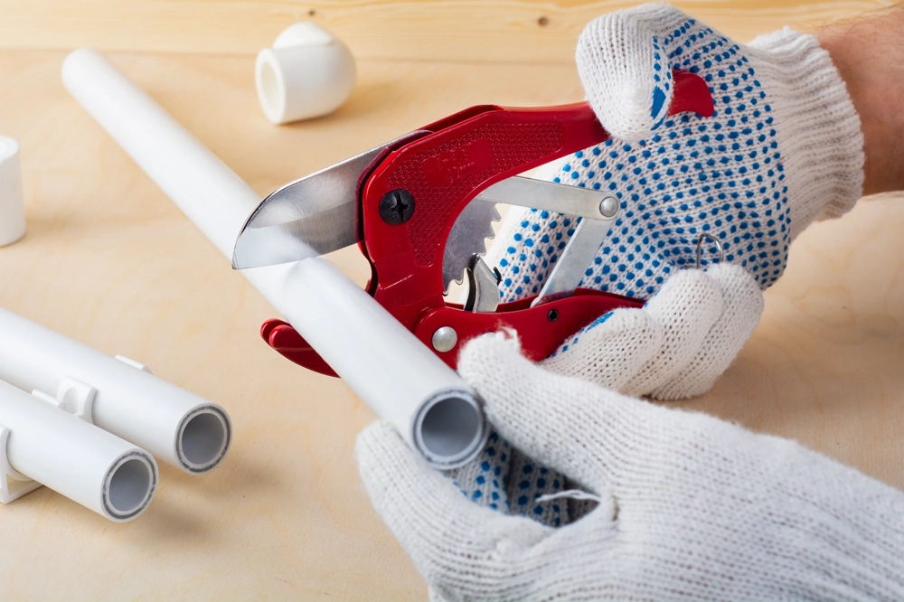 Obcinanie rury PCV przy pomocy nożyc ręcznych w rękawicach podczas prac hydraulicznych Hydraulik